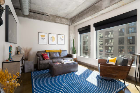 Interior of a contemporary living room with a leather sofa, blue striped rug, and large windows.