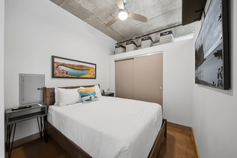 Modern loft bedroom featuring a concrete ceiling, white bed linens, nature artwork, and minimalist furniture.