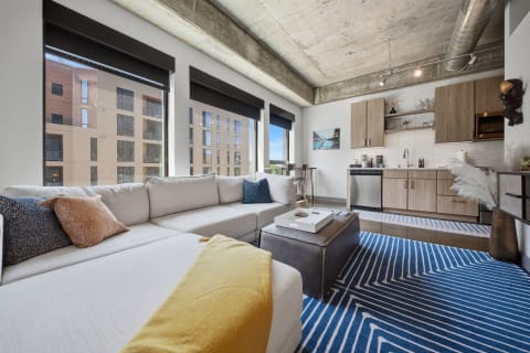 A spacious modern loft with floor-to-ceiling windows, a cozy sectional sofa, and a sleek kitchenette, showcasing an industrial-chic design.