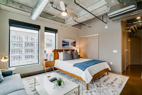 Modern industrial bedroom featuring a large bed, gray sofa, and large windows.