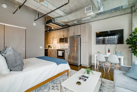Interior view of a modern studio apartment featuring a bed, kitchen area, and dining space.