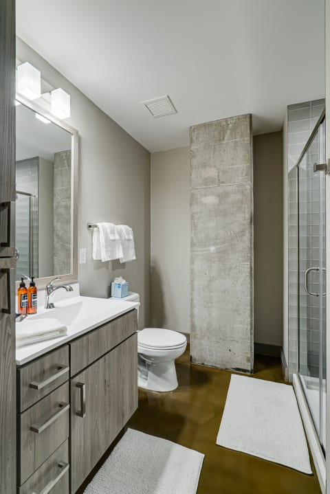 Modern bathroom with a glass shower, concrete pillar, and wooden vanity.