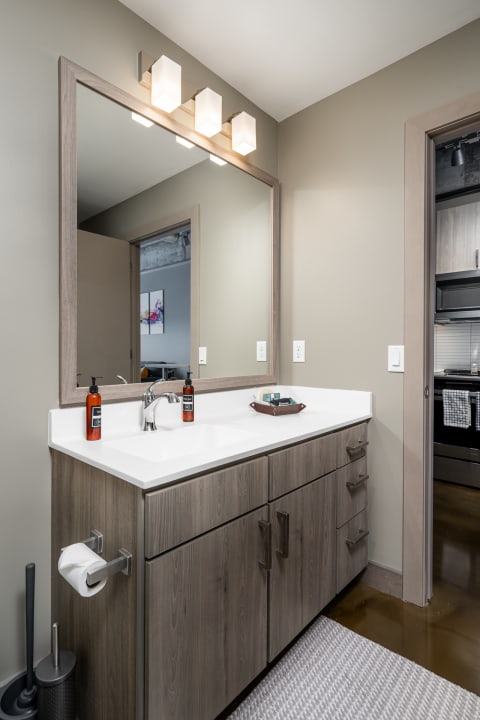 Modern bathroom with a light wood vanity and mirror, displaying amber soap bottles and a decorative tray.