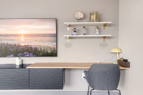 A minimalistic workspace featuring a beach sunset photo, a desk with decorative shelves, and a stylish lamp.