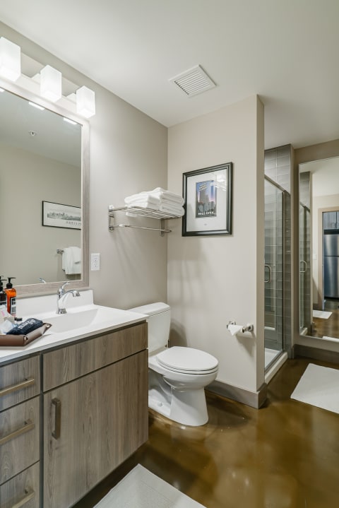 A sleek bathroom featuring a white sink, wooden vanity, glass shower, and neatly arranged towels.
