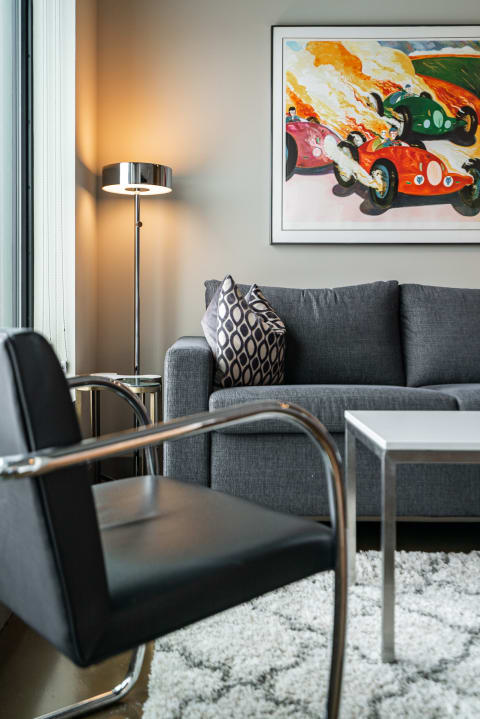 A contemporary living room with a gray sofa, black chair, wall art, and a floor lamp.