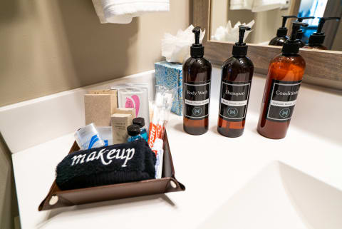 A bathroom countertop featuring toiletries including body wash, shampoo, conditioner, and a makeup towel.