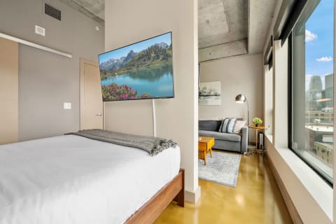 Modern studio apartment with a bed, TV displaying a landscape, and a cozy living space.