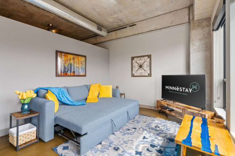 Living room featuring a blue sofa with yellow accents, a bouquet of tulips, and a TV with a logo.