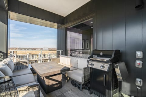 Modern balcony with seating and grill overlooking the city skyline.