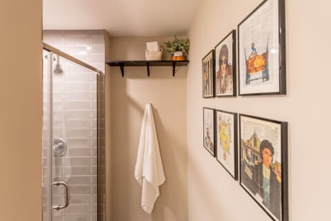 Stylish corner of a bathroom featuring a glass shower, a towel on a shelf, and framed artworks on the wall.