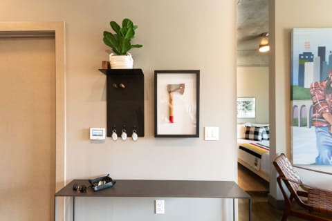 Contemporary entryway with a plant on a shelf, key hooks, framed axe art, and a narrow table with sunglasses.