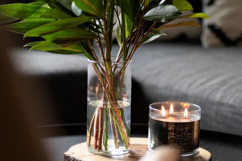 A clear vase with green leaves and a candle beside it on a wooden surface.
