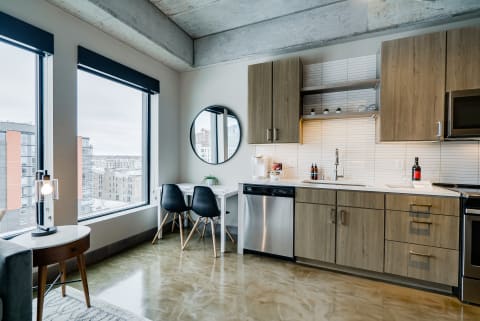 A sleek kitchen in a modern apartment featuring wooden cabinets, stainless steel appliances, and large windows.