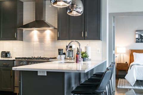 Modern kitchen with dark cabinets, white countertop, and a glimpse of a bedroom.