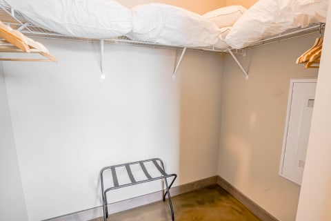 A small closet with white comforters on a shelf and wooden hangers on a rod.