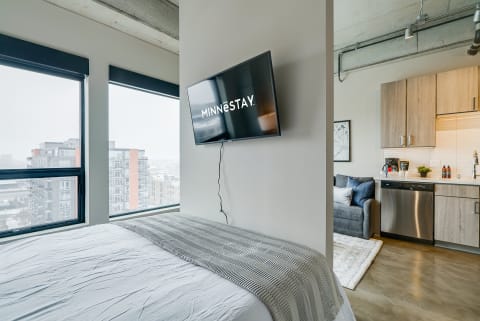 Interior of a contemporary studio apartment featuring a bed, TV, and kitchen area, with snowy views outside.