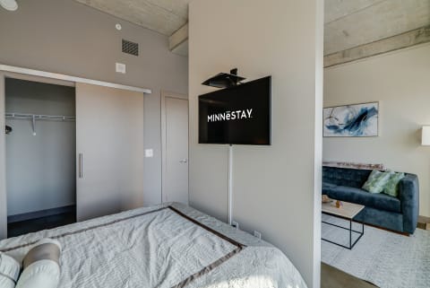 Modern bedroom with a bed, TV, and dark blue couch.