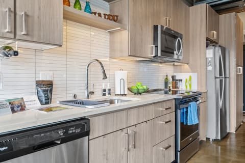 Modern kitchen with wooden cabinets, colorful glass bottles, and fresh green apples on the counter.