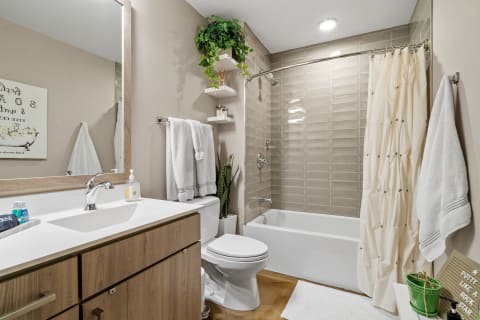 A modern bathroom featuring a white vanity, a large mirror, and a bathtub with taupe tiles.