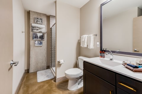 Modern bathroom with a white toilet, dark cabinetry, large mirror, and glass shower.