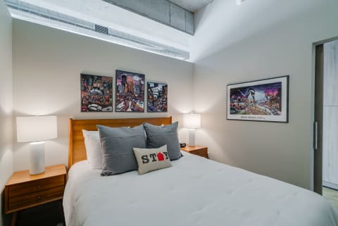Modern bedroom featuring a bed with gray pillows and cityscape art on the walls.
