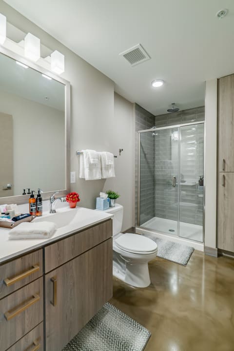 Contemporary bathroom featuring a glass shower, wooden cabinetry, and stylish lighting.