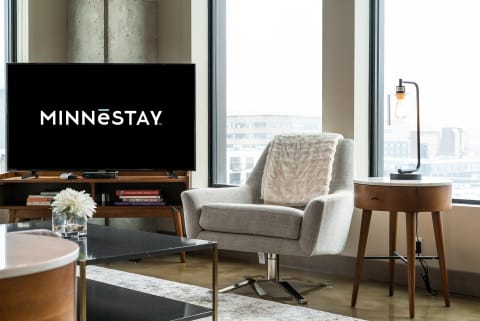 Cozy living space with an armchair, side table, lamp, and a television displaying the MINNESTAY logo.
