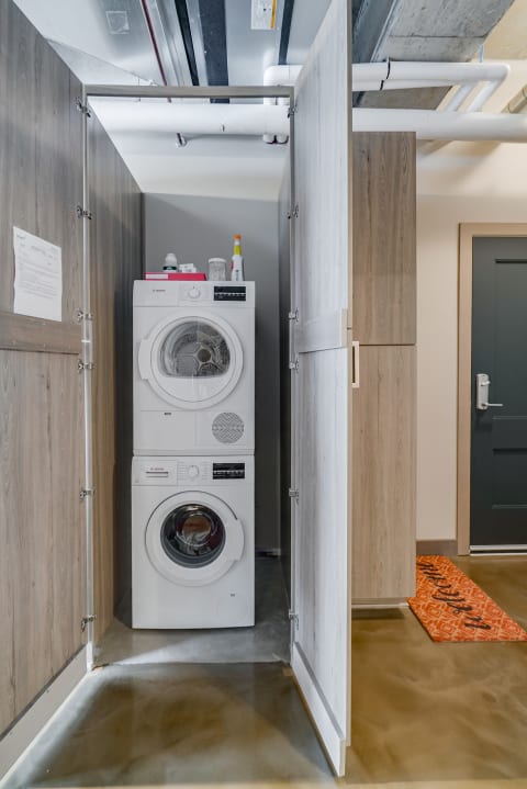 Laundry area with stacked washer and dryer, surrounded by wooden doors and a polished concrete floor.