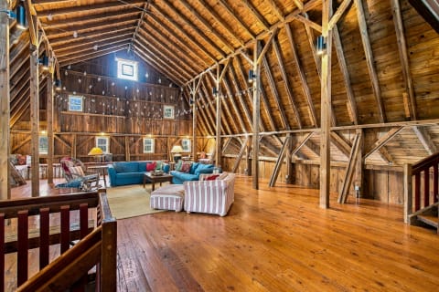 Interior of a barn-style living room with wooden beams, cozy furniture, and twinkling lights.