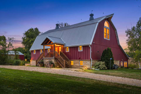 A stunning barn-style property with red siding and a metal roof, featuring a covered entry and surrounded by greenery during twilight.