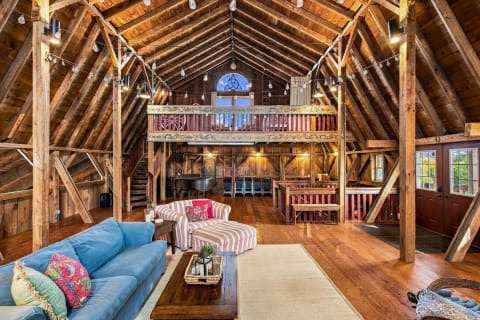 Interior of a barn-style retreat showcasing wooden beams, cozy seating, and a loft.