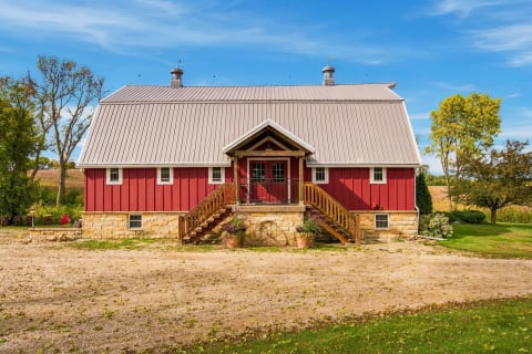 A red barn with a stone foundation and wooden staircases set in a picturesque rural landscape.