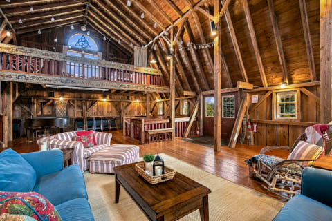 Rustic barn interior with soaring wooden beams, plush seating, and warm ambient lighting.