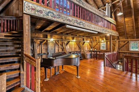 Interior view of a timber barn loft with a grand piano and hand-painted beams.