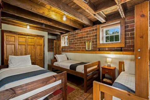 A cabin-style bedroom with wooden beams, brick walls, two beds, and a bedside table with a lamp.
