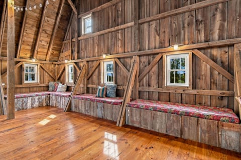 A cozy loft with wooden walls, window seats, and lush, colorful cushions.