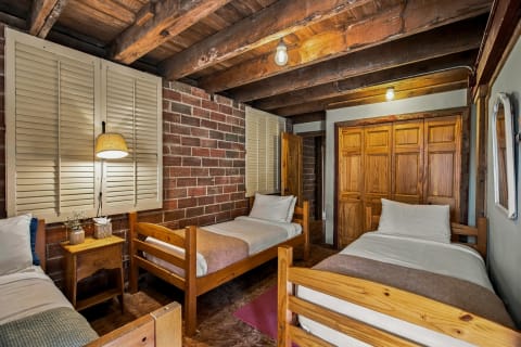 A cozy rustic retreat with three twin beds, exposed beams, and warm brick walls, inviting relaxation.