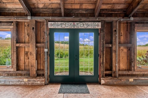 Interior view of a rustic barn-style entrance featuring green glass doors and wooden walls, looking out onto lush fields.