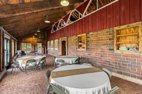 Interior view of a rustic gathering area featuring circular tables, wooden beams, and exposed brick walls.