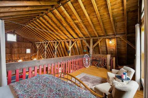 Interior view of a rustic barn loft with wood beams, red accents, and cozy seating.