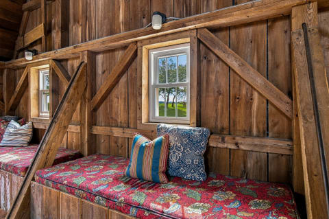 Cozy barn interior with floral cushions overlooking green fields through a window.