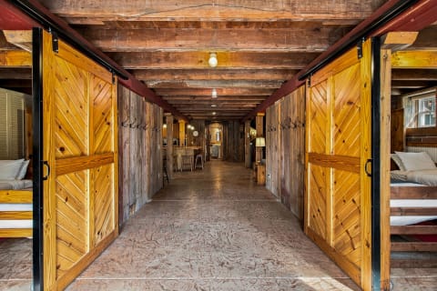 Interior view of a barn-style space featuring wooden beams and sliding doors, leading to a rustic communal area.