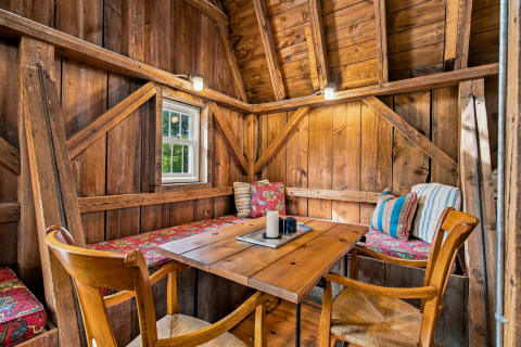 A cozy wooden nook with a table and cushions, featuring warm wooden walls and soft lighting.
