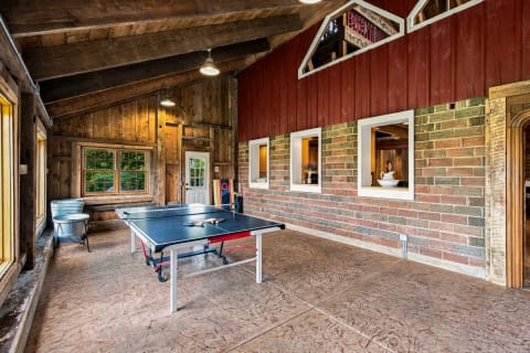 Interior view of a rustic game room with a ping pong table, wooden beams, and brick walls.