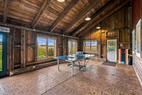 Inside a rustic game room with exposed beams and countryside views, featuring a ping pong table and bean bag toss game.