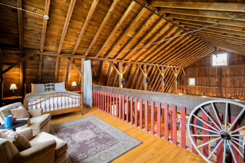 A rustic loft bedroom featuring a cozy bed, wooden beams, and a plush seating area adorned with vintage decor.