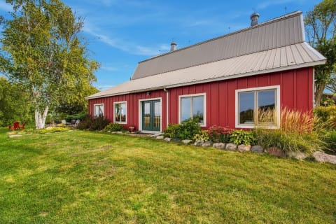 A red barn-style house with a metal roof, surrounded by green lawns and landscaped gardens under a clear blue sky.