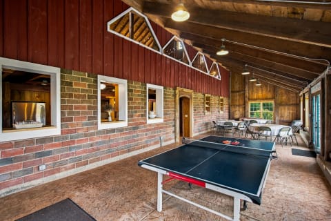 Interior view of a recreational barn featuring a ping pong table, dining tables, and rustic decor.