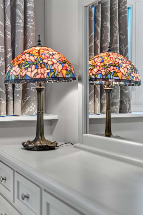 A stained-glass lamp with floral patterns reflects in a mirror, accompanied by patterned curtains.